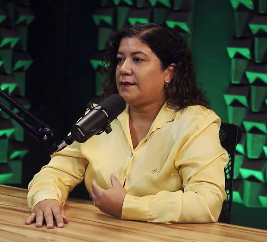 Jussara Fialho, de camisa amarela, fala ao microfone no estúdio do Unicast.